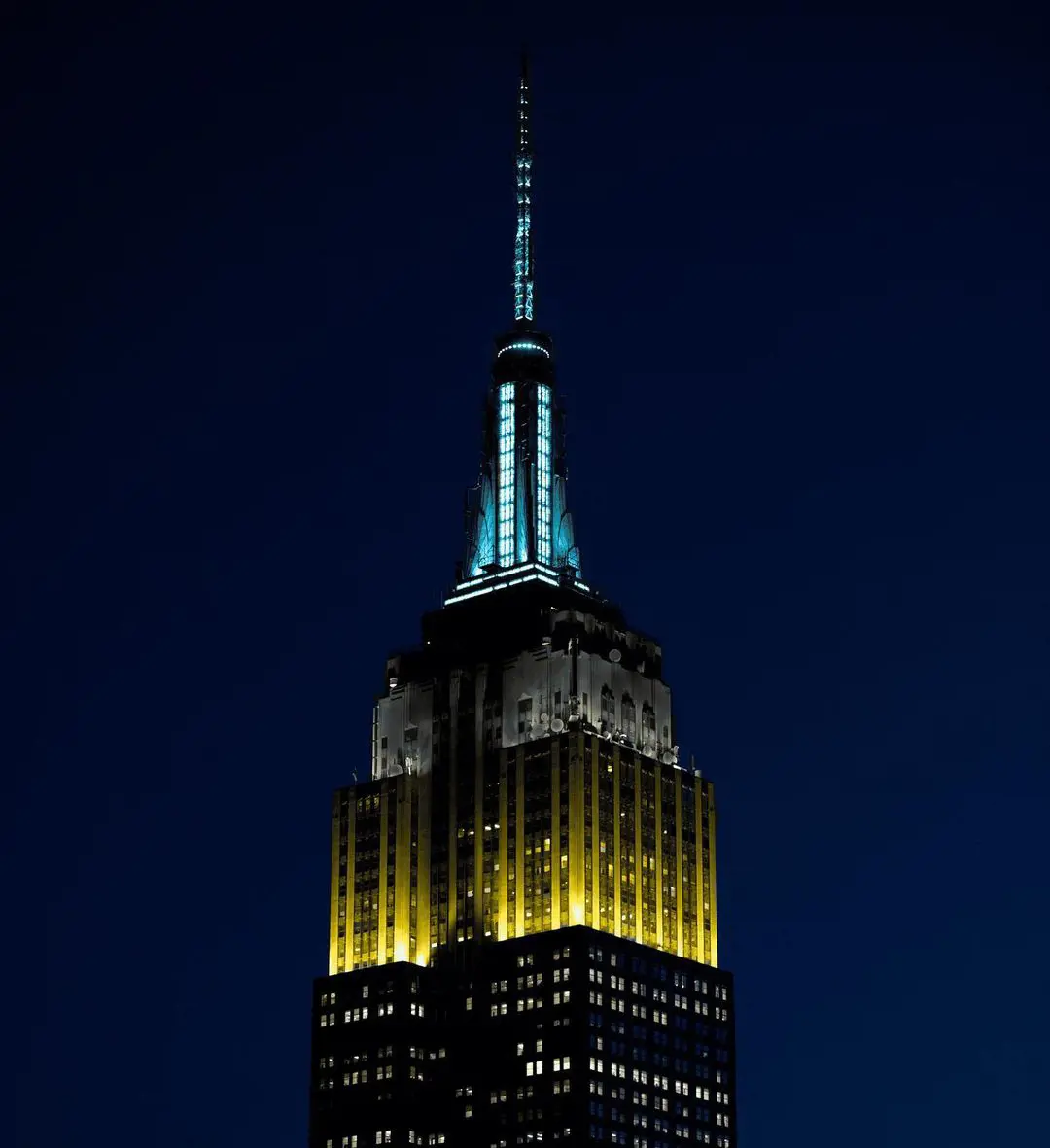 The Empire State building shining in Gold, Black, and Aqua.
